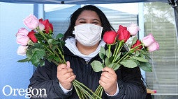 image of individual in a face mask holding stemmed roses in each hand